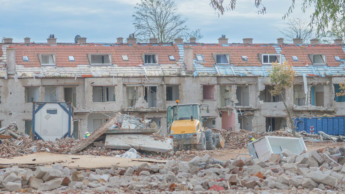 Een rij woningen half afgebroken, met puin en een laadschop op de voorgrond