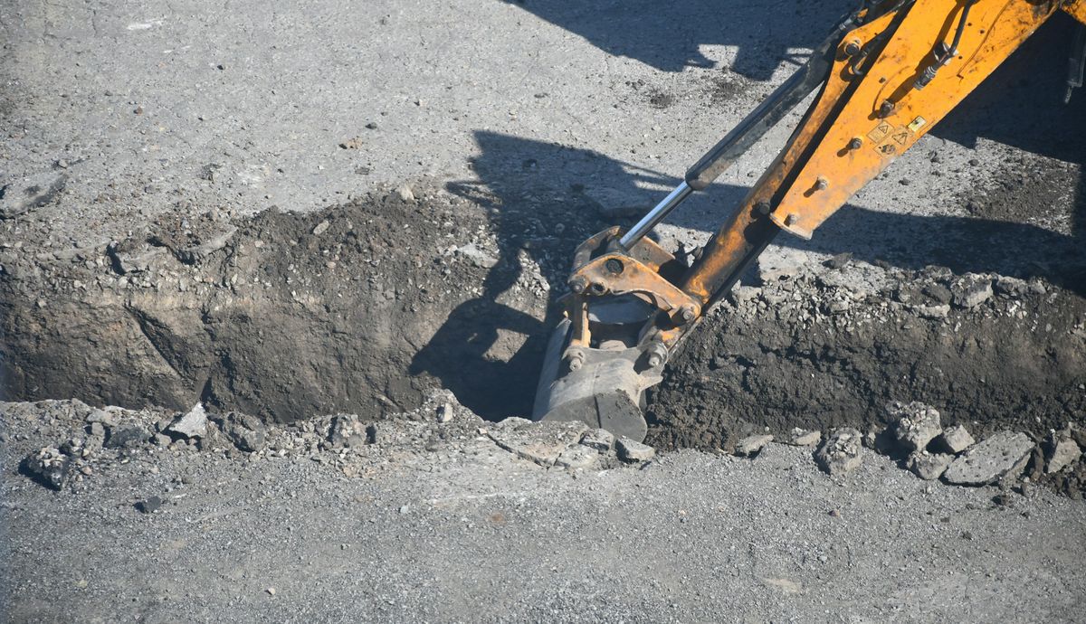 De bak van een graafmachine graaft een sleuf door een verharde oprit
